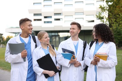 Photo of Medical students in uniforms with backpacks and notebooks outdoors, selective focus