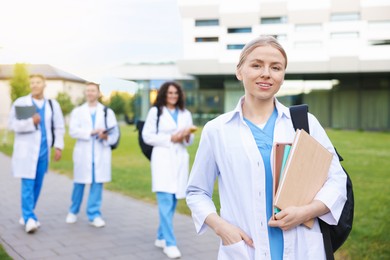 Photo of Medical student in uniform with backpack, tablet and notebooks outdoors, selective focus