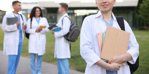 Photo of Medical student in uniform with backpack, tablet and notebooks outdoors, selective focus
