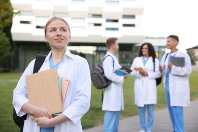 Photo of Medical student in uniform with backpack, tablet and notebooks outdoors, selective focus