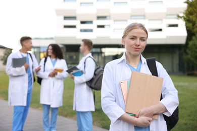 Photo of Medical student in uniform with backpack, tablet and notebooks outdoors, selective focus