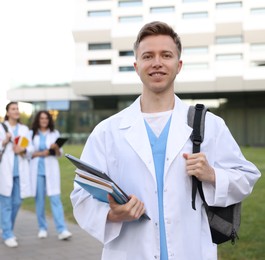 Photo of Medical student in uniform with backpack, laptop and notebooks outdoors, selective focus