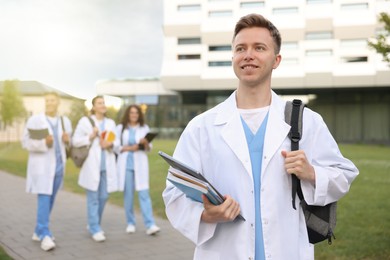 Photo of Medical student in uniform with backpack, laptop and notebooks outdoors, selective focus
