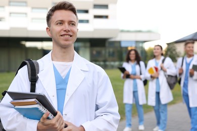 Photo of Medical student in uniform with backpack, laptop and notebooks outdoors, selective focus