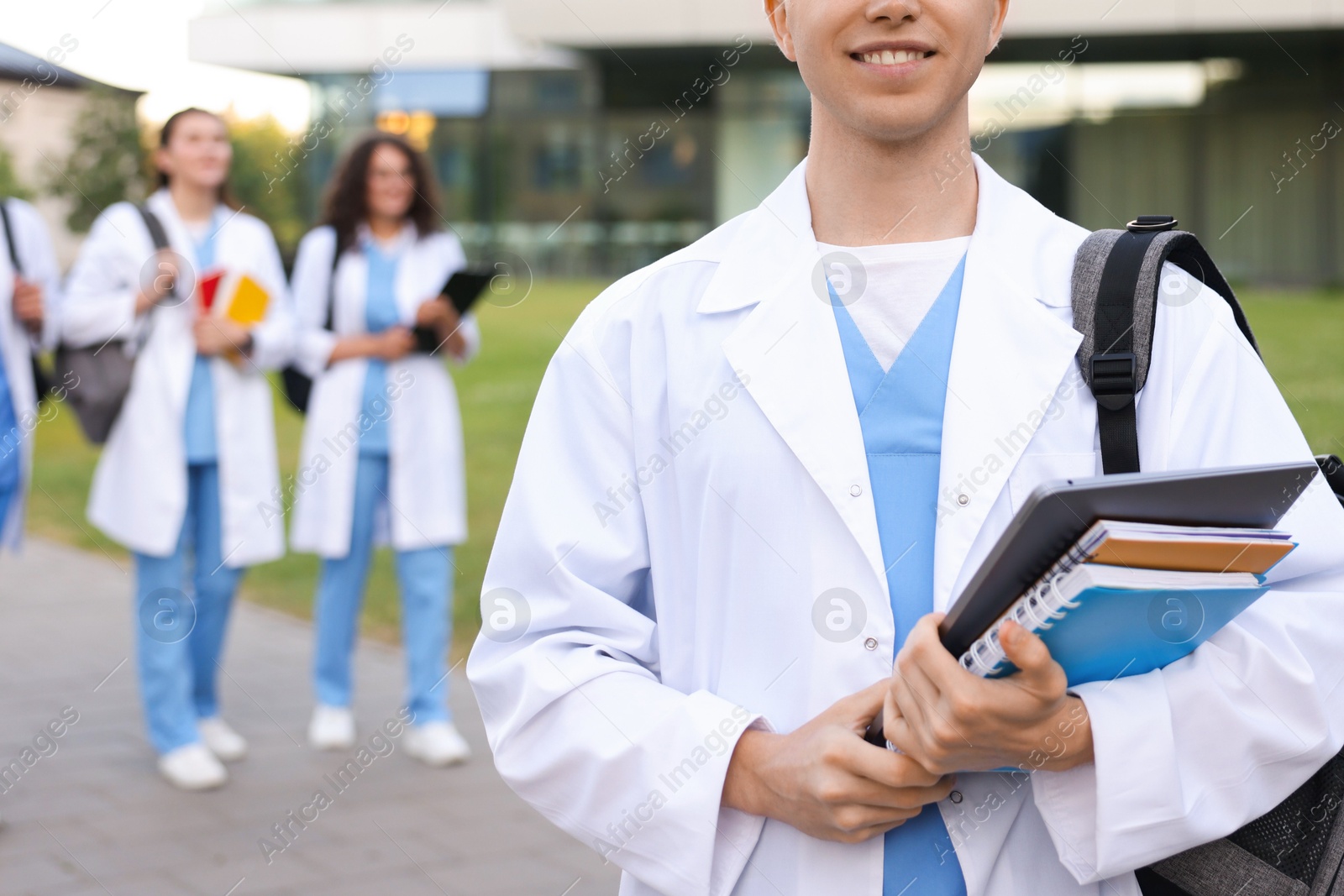 Photo of Medical student in uniform with backpack, laptop and notebooks outdoors, selective focus