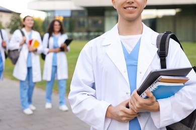 Photo of Medical student in uniform with backpack, laptop and notebooks outdoors, selective focus