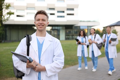 Photo of Medical student in uniform with backpack, laptop and notebooks outdoors, selective focus