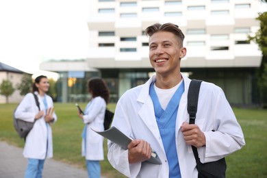Photo of Medical student in uniform with backpack and notebook outdoors, selective focus