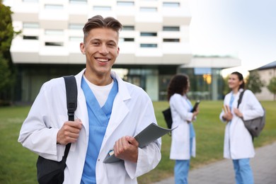 Photo of Medical student in uniform with backpack and notebook outdoors, selective focus