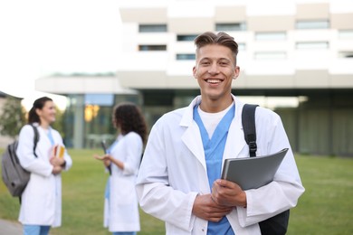 Photo of Medical student in uniform with backpack and notebook outdoors, selective focus