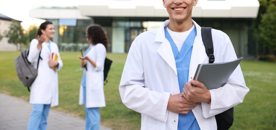 Photo of Medical student in uniform with backpack and notebook outdoors, selective focus