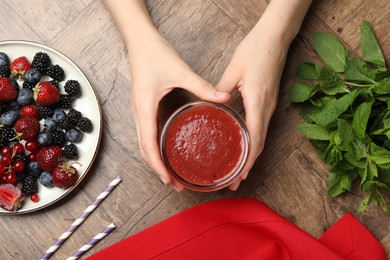Photo of Superfood. Woman with tasty smoothie and ingredients at wooden table, top view