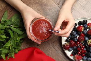 Photo of Superfood. Woman with tasty smoothie and ingredients at wooden table, top view
