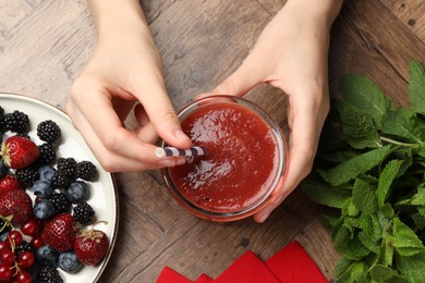 Photo of Superfood. Woman with tasty smoothie and ingredients at wooden table, top view