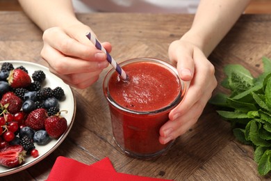 Photo of Superfood. Woman with tasty smoothie and ingredients at wooden table, closeup