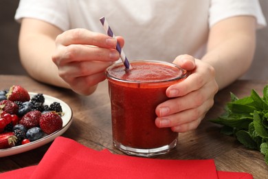 Photo of Superfood. Woman with tasty smoothie and ingredients at wooden table, closeup