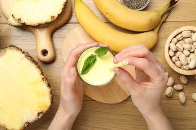 Photo of Superfood. Woman with tasty smoothie and ingredients at wooden table, top view