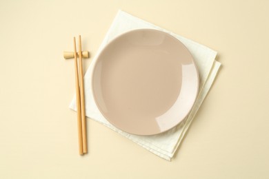 Photo of Stylish plate, chopsticks and napkin on beige background, flat lay