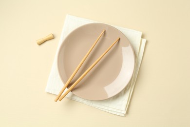 Photo of Stylish plate, chopsticks and napkin on beige background, flat lay