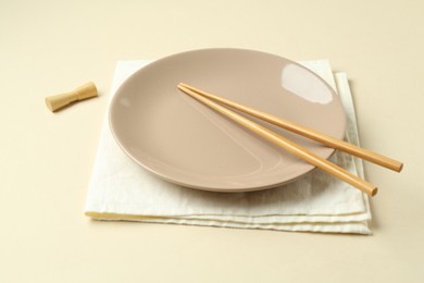 Photo of Stylish plate, chopsticks and napkin on beige background, closeup
