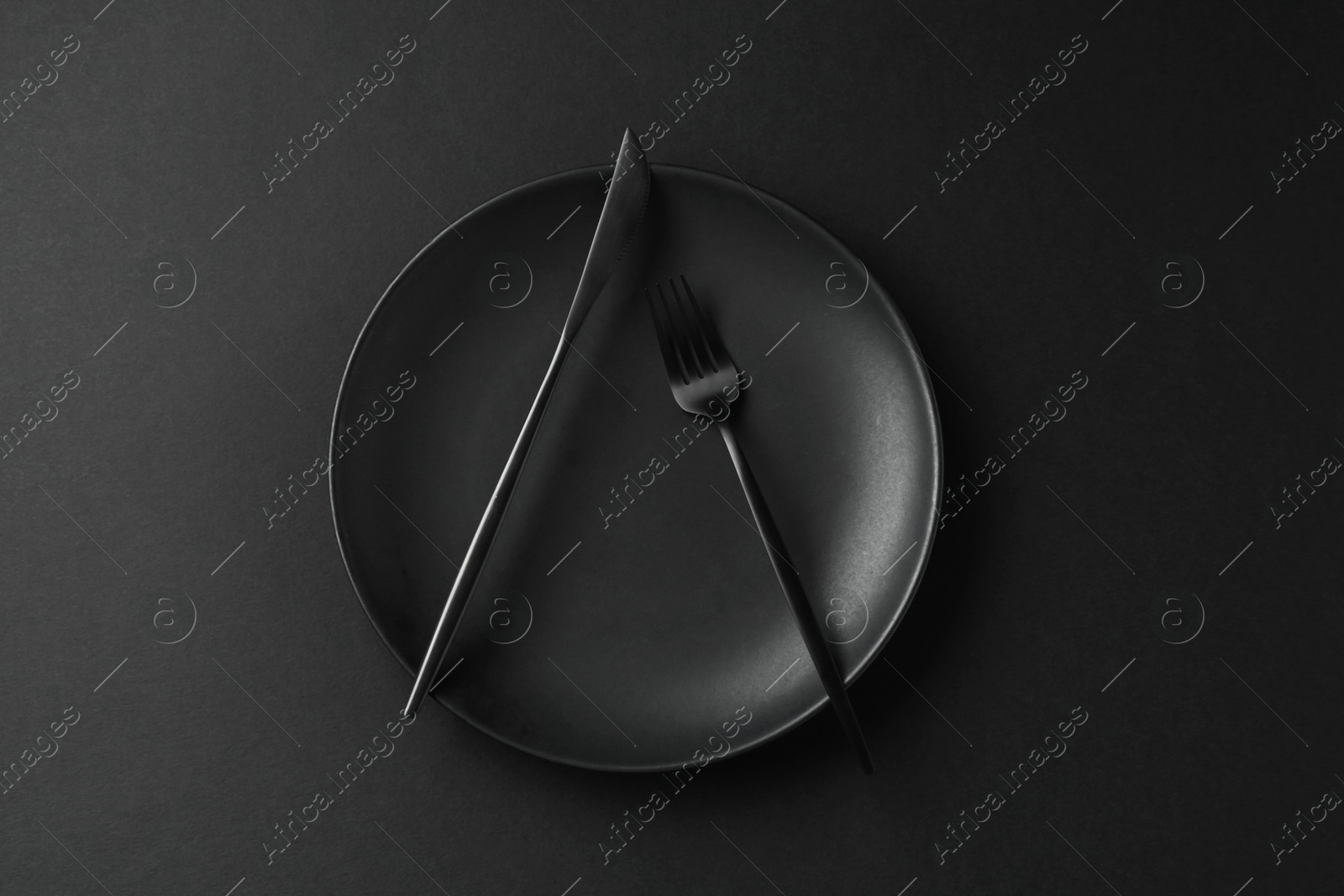 Stylish plate and cutlery on black background, top view Photo of Stylish plate and cutlery on black background, top view