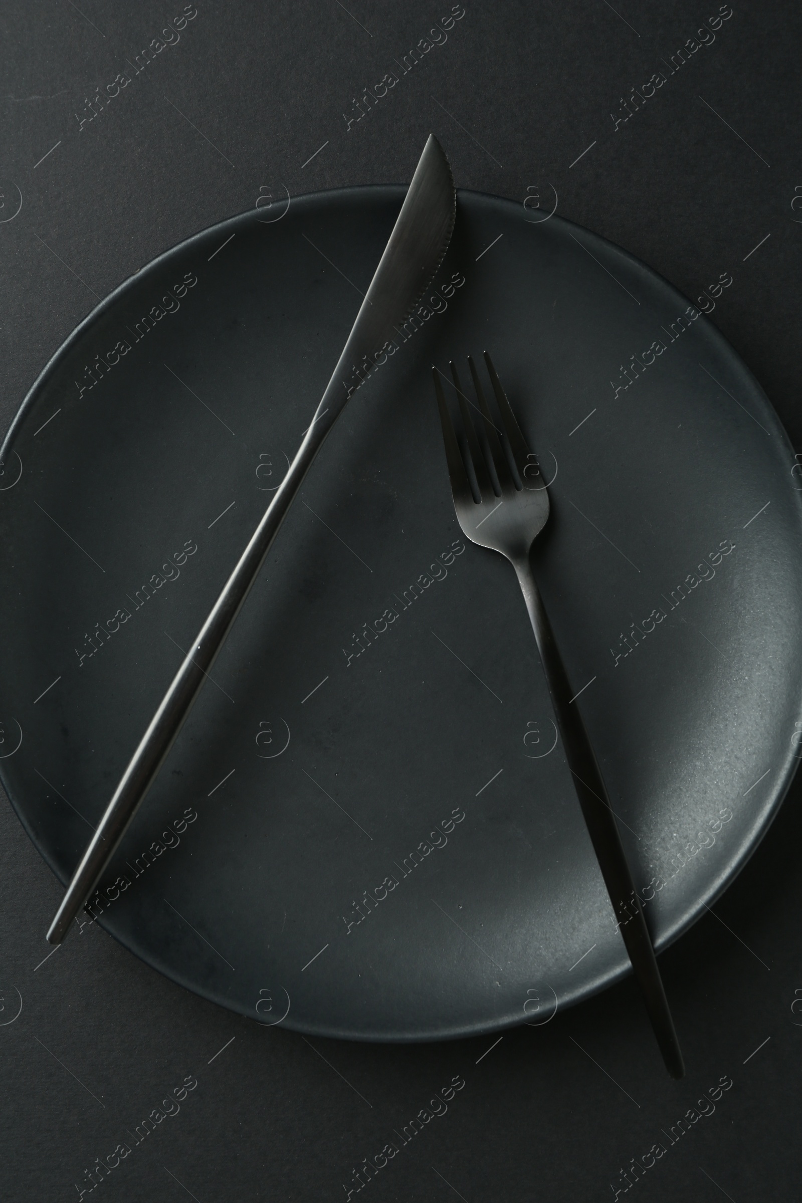 Stylish plate and cutlery on black background, top view Photo of Stylish plate and cutlery on black background, top view