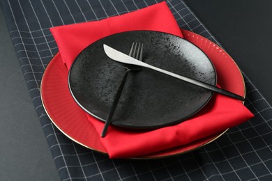 Photo of Stylish plates, cutlery and napkins on black background, closeup