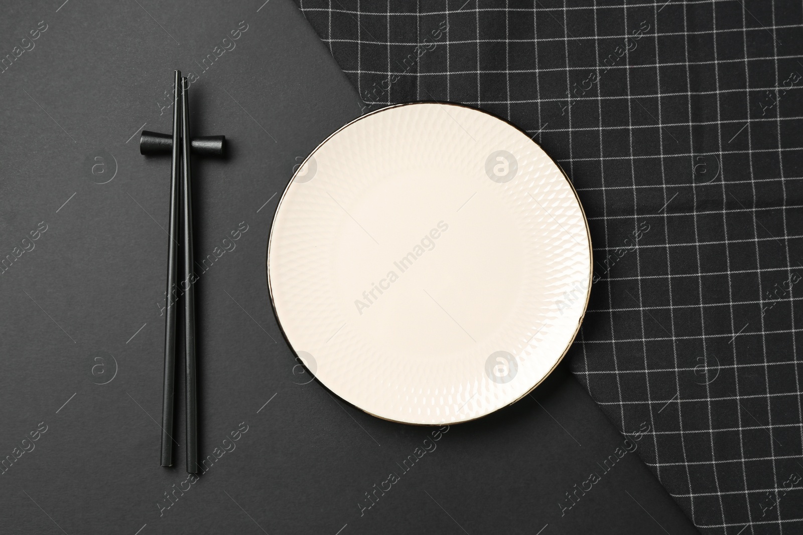 Stylish plate, chopsticks and napkin on black background, flat lay Photo of Stylish plate, chopsticks and napkin on black background, flat lay