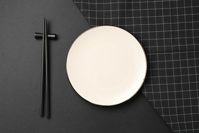 Photo of Stylish plate, chopsticks and napkin on black background, flat lay