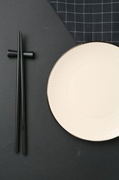 Photo of Stylish plate, chopsticks and napkin on black background, flat lay