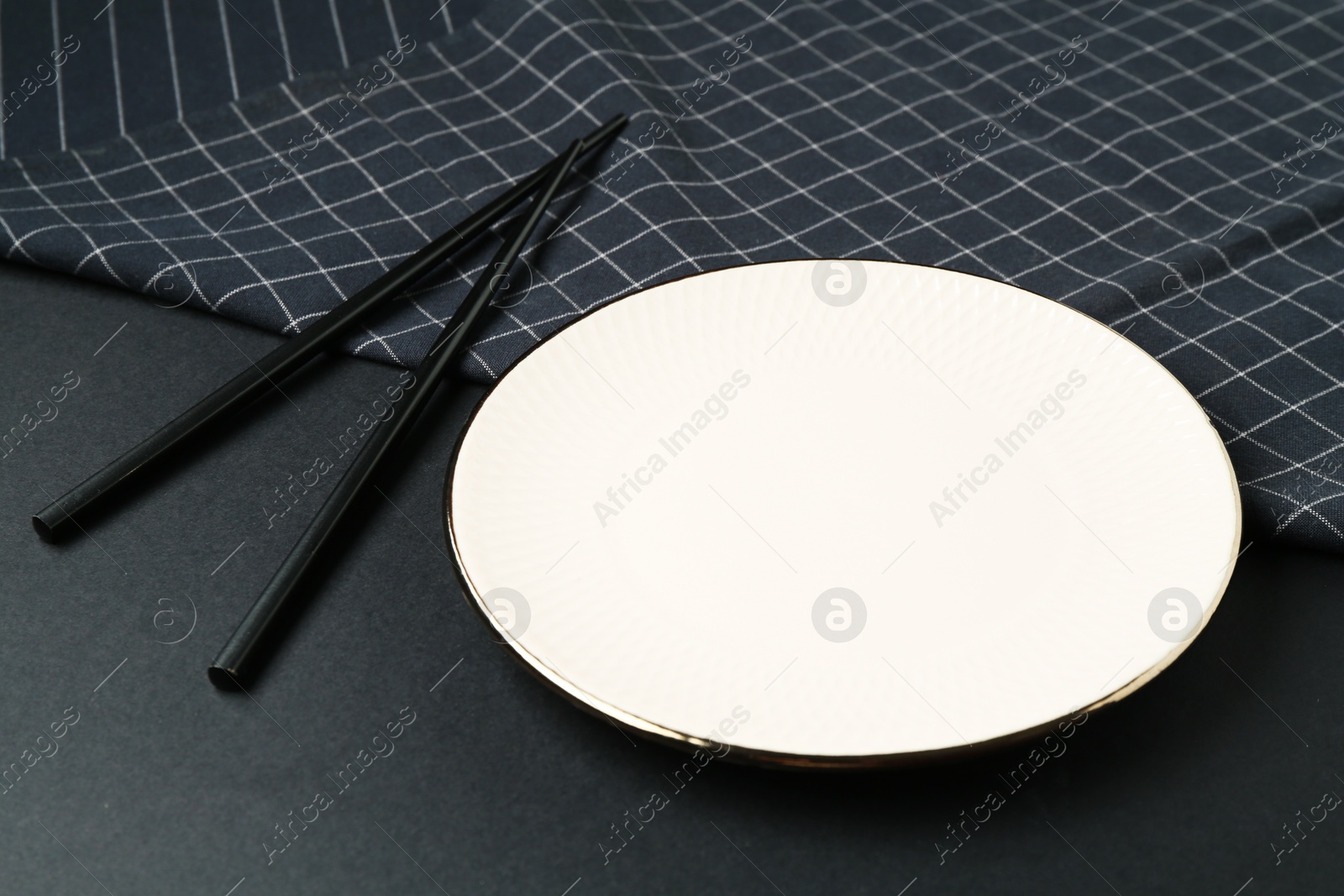 Stylish plate, chopsticks and napkin on black background, closeup Photo of Stylish plate, chopsticks and napkin on black background, closeup