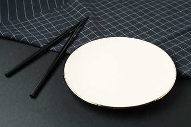 Photo of Stylish plate, chopsticks and napkin on black background, closeup