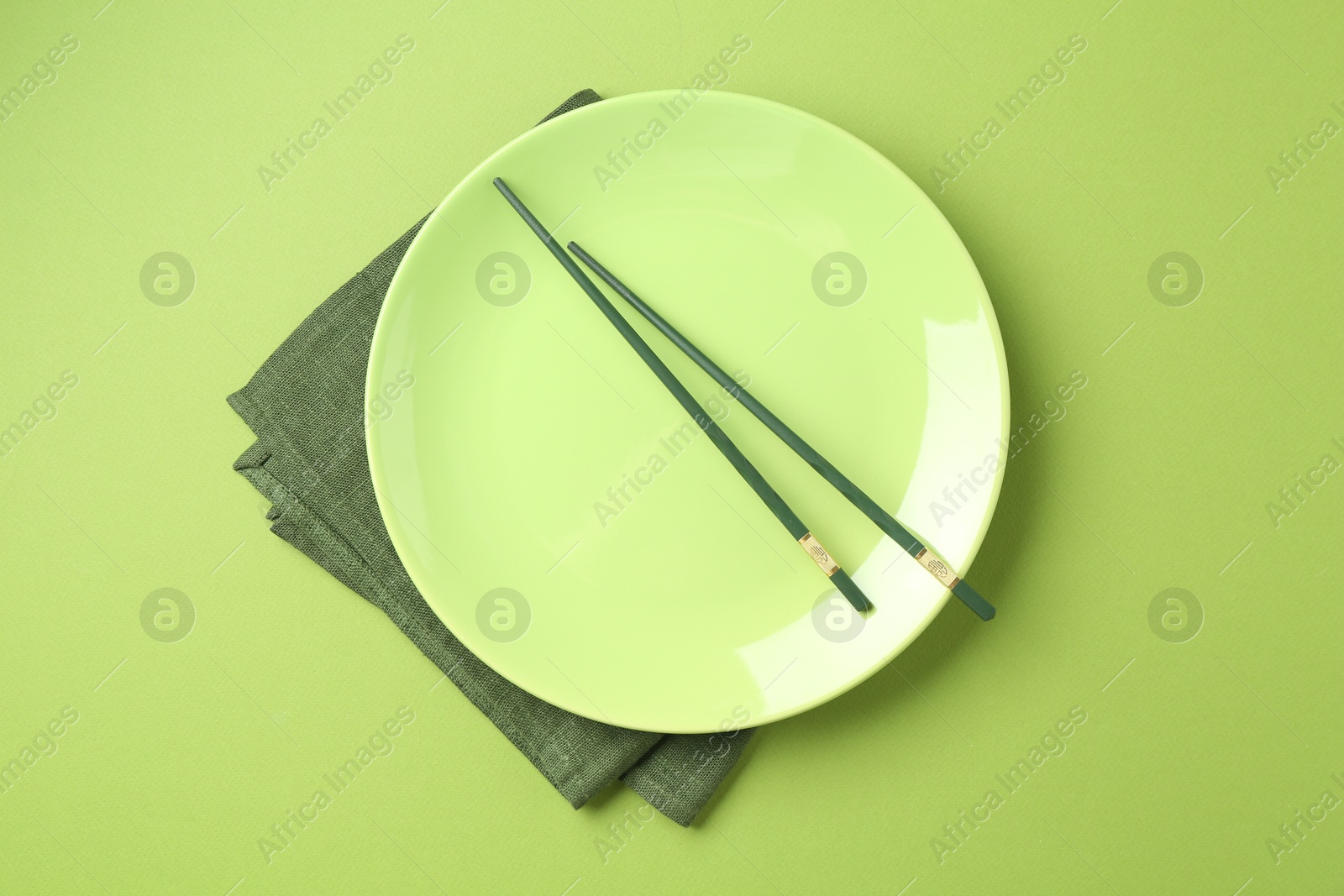 Stylish plate, chopsticks and napkin on green background, top view Photo of Stylish plate, chopsticks and napkin on green background, top view