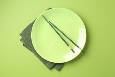 Photo of Stylish plate, chopsticks and napkin on green background, top view