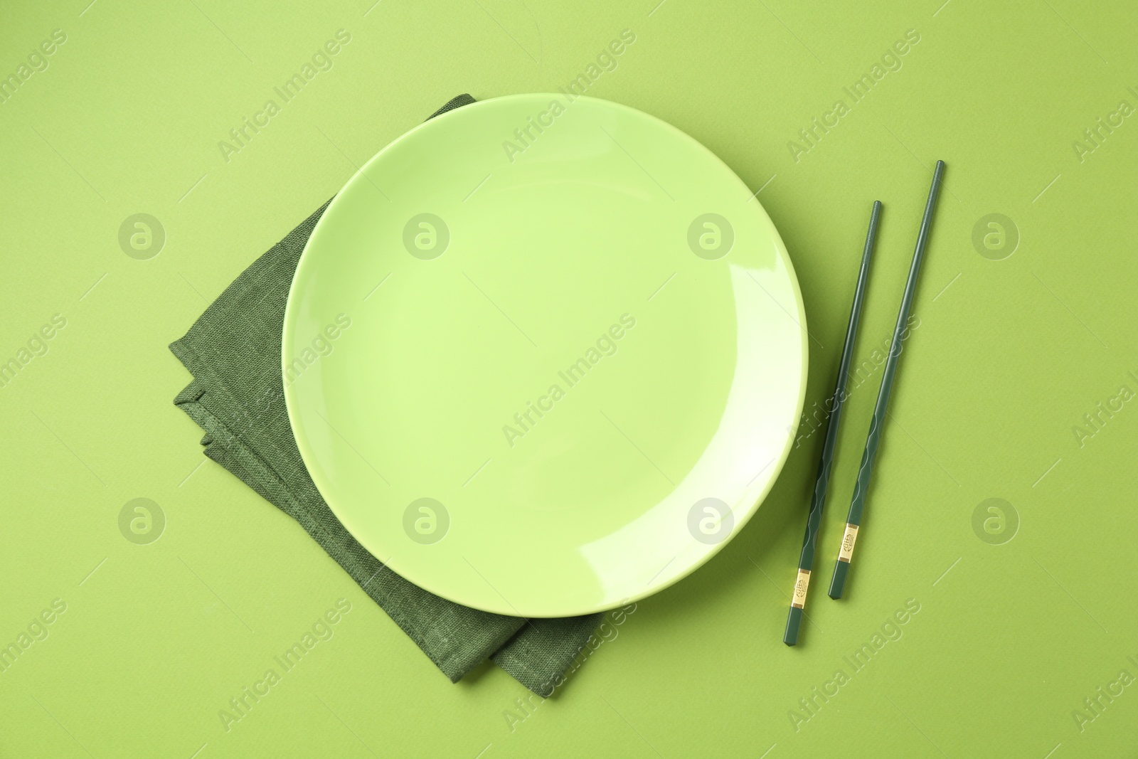 Stylish plate, chopsticks and napkin on green background, flat lay Photo of Stylish plate, chopsticks and napkin on green background, flat lay