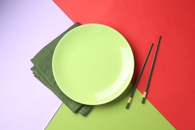 Photo of Stylish plate, chopsticks and napkin on color background, flat lay