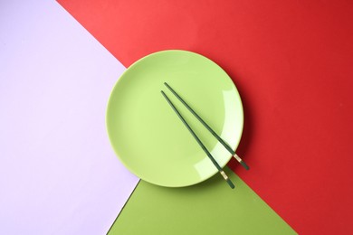 Photo of Stylish plate and chopsticks on color background, top view