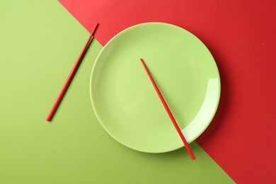 Photo of Stylish plate and chopsticks on color background, flat lay