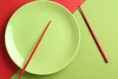 Photo of Stylish plate and chopsticks on color background, flat lay
