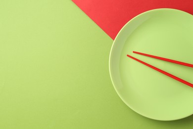 Photo of Stylish plate and chopsticks on color background, top view. Space for text
