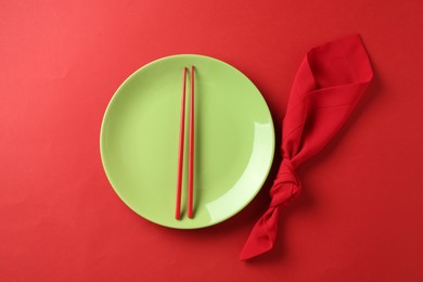 Photo of Stylish plate, chopsticks and napkin on red background, flat lay