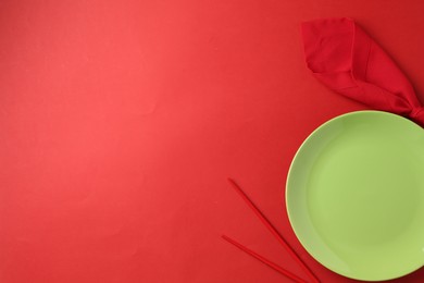 Photo of Stylish plate, chopsticks and napkin on red background, flat lay. Space for text