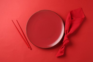 Photo of Stylish plate, chopsticks and napkin on red background, flat lay
