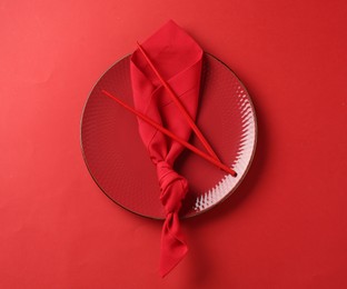 Photo of Stylish plate, chopsticks and napkin on red background, top view