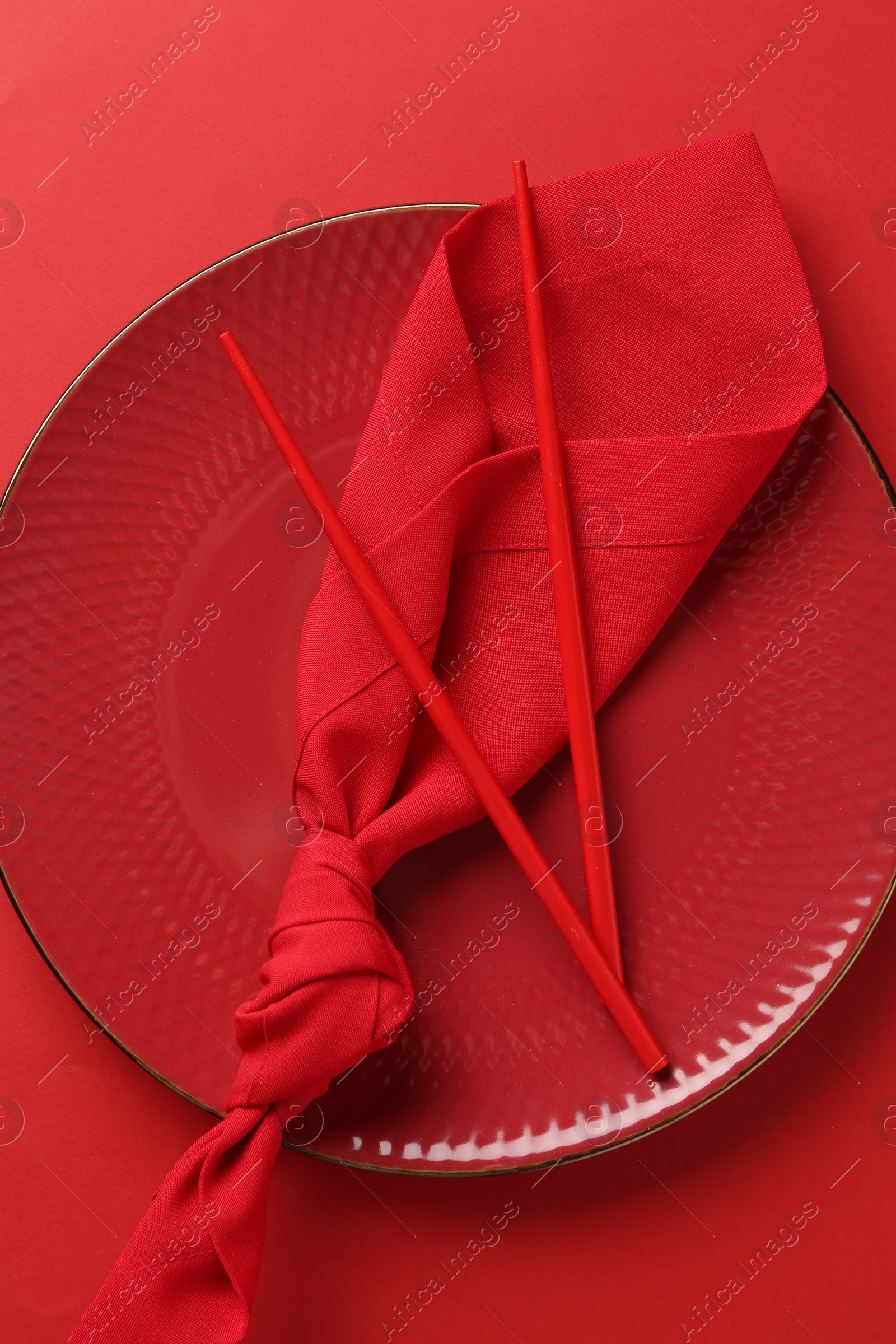 Stylish plate, chopsticks and napkin on red background, top view Photo of Stylish plate, chopsticks and napkin on red background, top view
