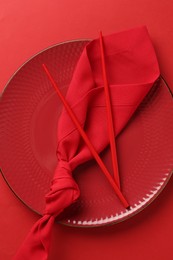 Photo of Stylish plate, chopsticks and napkin on red background, top view