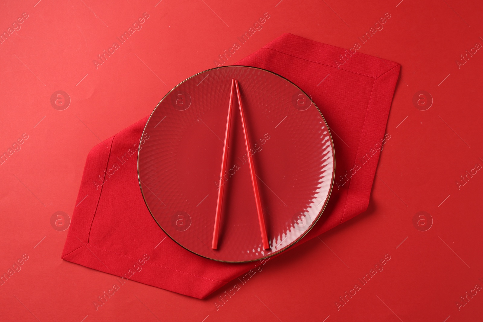 Stylish plate, chopsticks and napkin on red background, top view Photo of Stylish plate, chopsticks and napkin on red background, top view