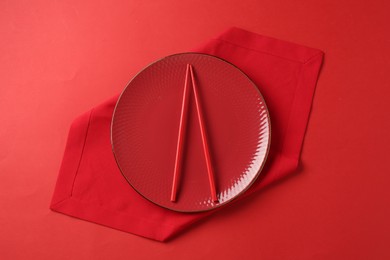 Photo of Stylish plate, chopsticks and napkin on red background, top view