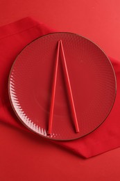 Photo of Stylish plate, chopsticks and napkin on red background, top view