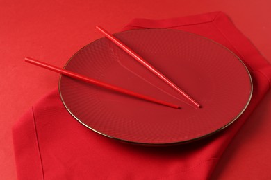 Photo of Stylish plate, chopsticks and napkin on red background, closeup